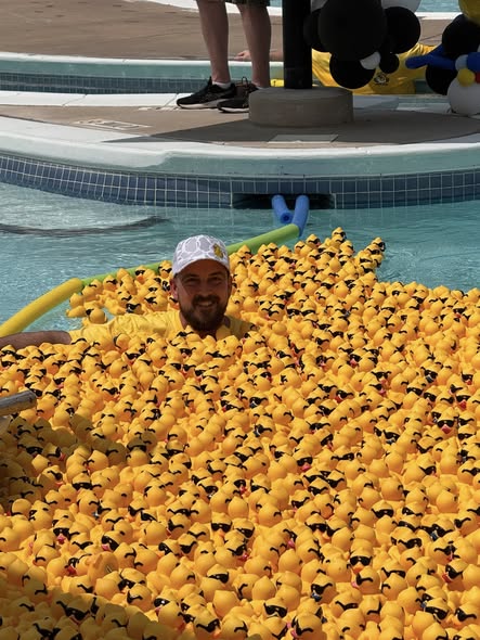 A volunteer surrounded by hundreds of yellow rubber ducks at the Arlington Sunrise Rotary duck race