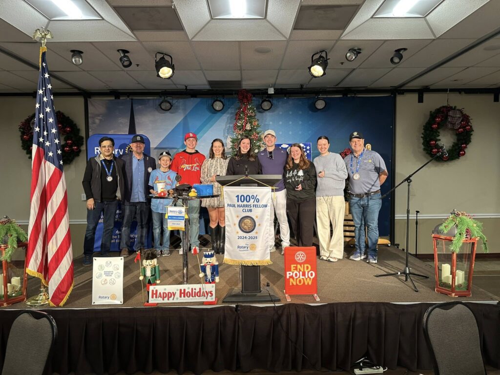 Arlington Sunrise Rotarians on stage in front of a Happy Holidays sign at a December meeting